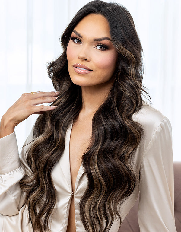 Model with long, wavy dark brown hair wearing a satin blouse.