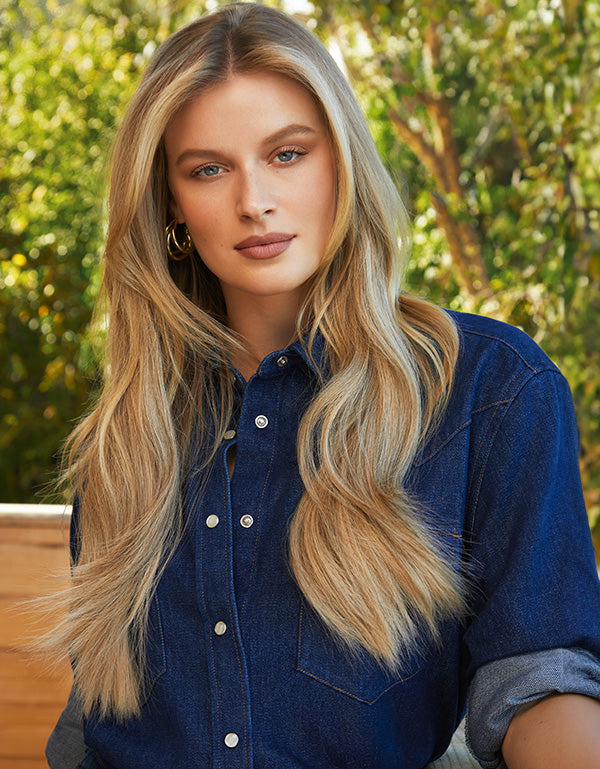 Model with long blonde hair wearing a denim shirt outdoors.